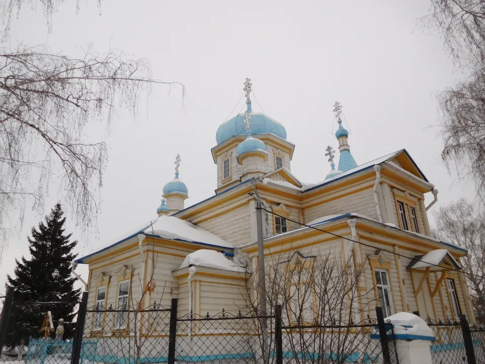 Деревянный храм с голубыми куполами зимой, за оградой