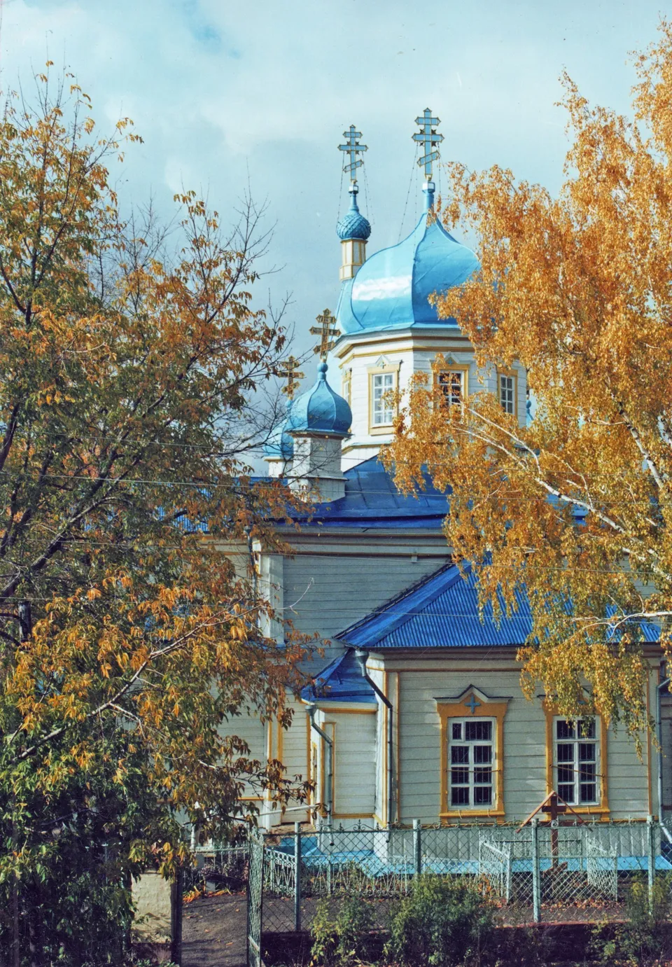 Деревянный храм с голубыми куполами осенью в жёлтой листве