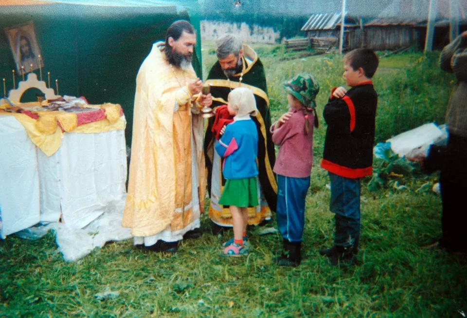 Священник служит молебен на сельском берегу, рядом дети и взрослые