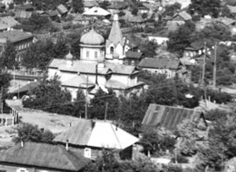 Чёрно-белый снимок сверху: деревянная купольная церковь с шатровой колокольней среди частных домов и деревьев