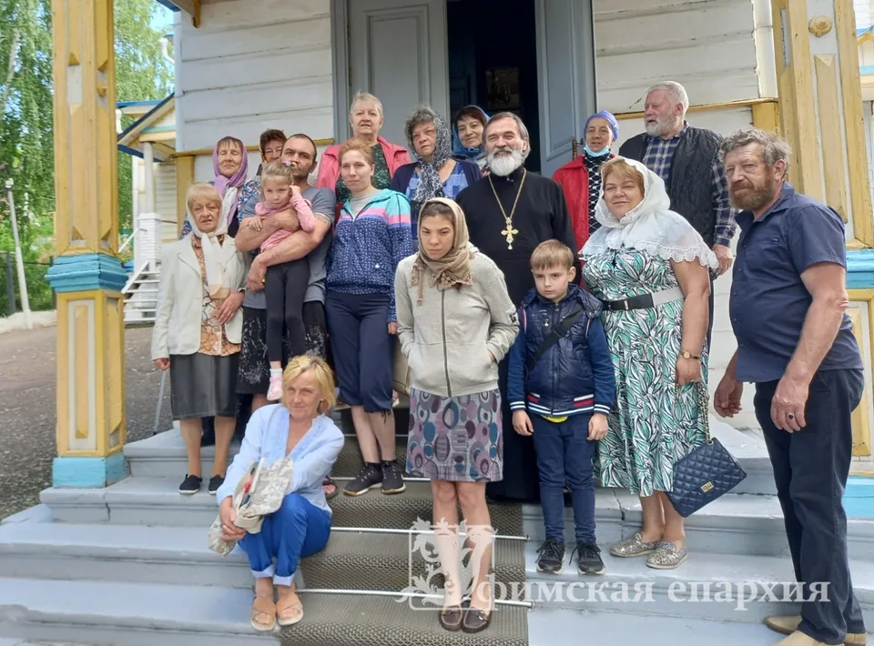 Группа взрослых и детей вместе со священником на резном деревянном крыльце храма