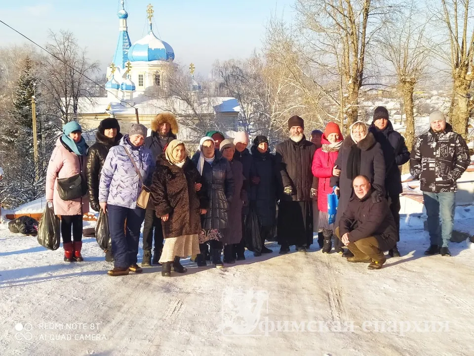 Группа взрослых и детей в зимней одежде со священником на фоне синекупольного храма